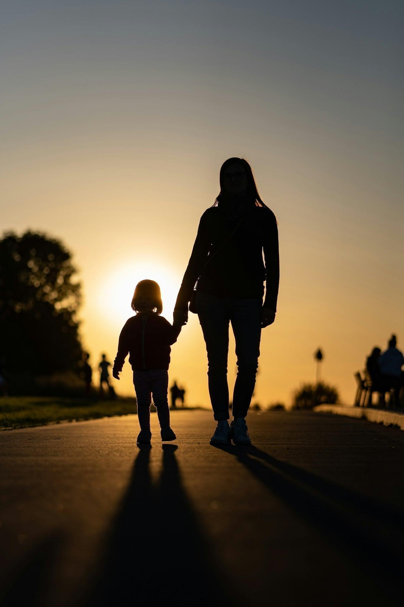 Caregiver walking hand in hand with a child at sunset